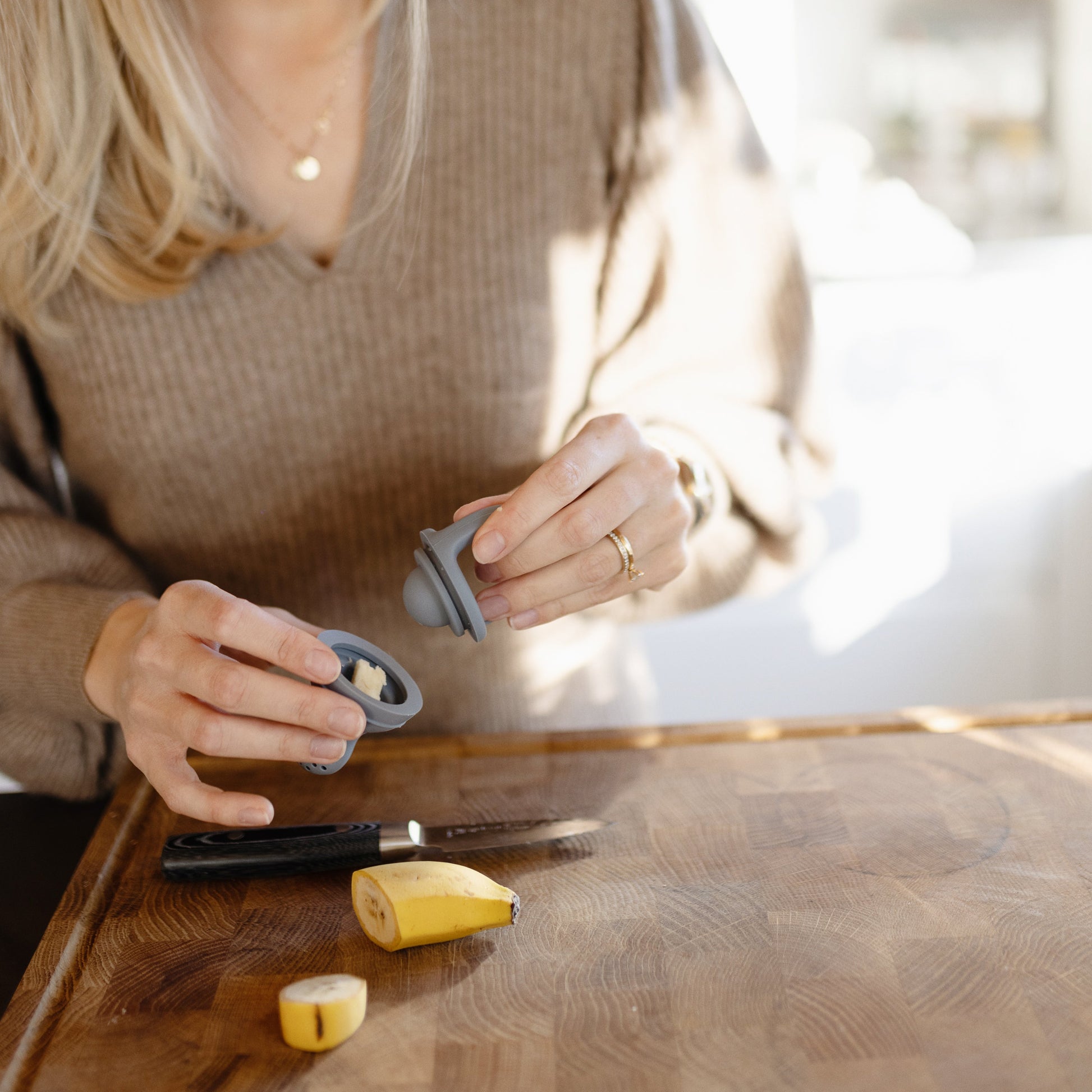 Person using a garlic press on a wooden cutting board with garlic and a knife.