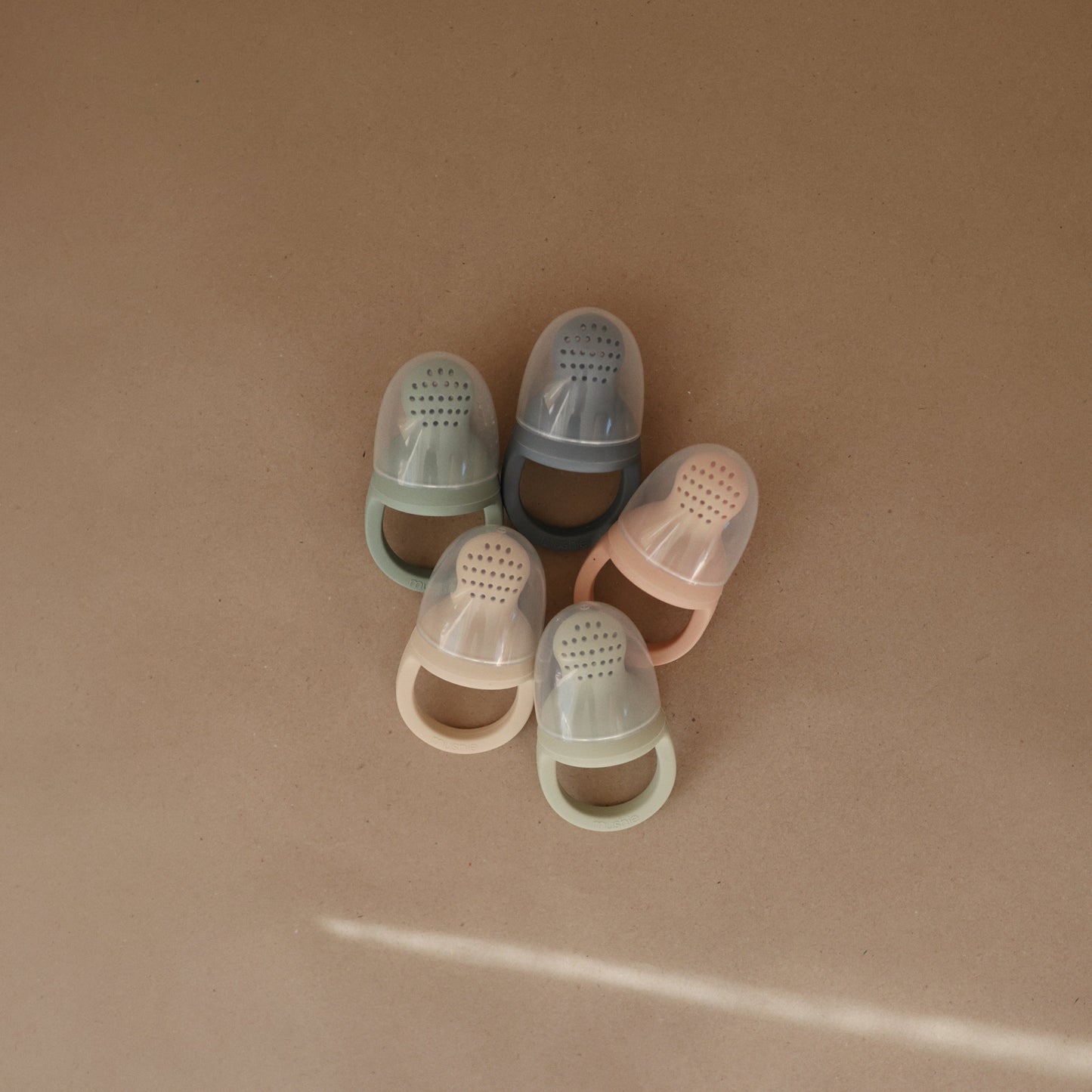 Set of five transparent baby shoes in various colors on a beige background