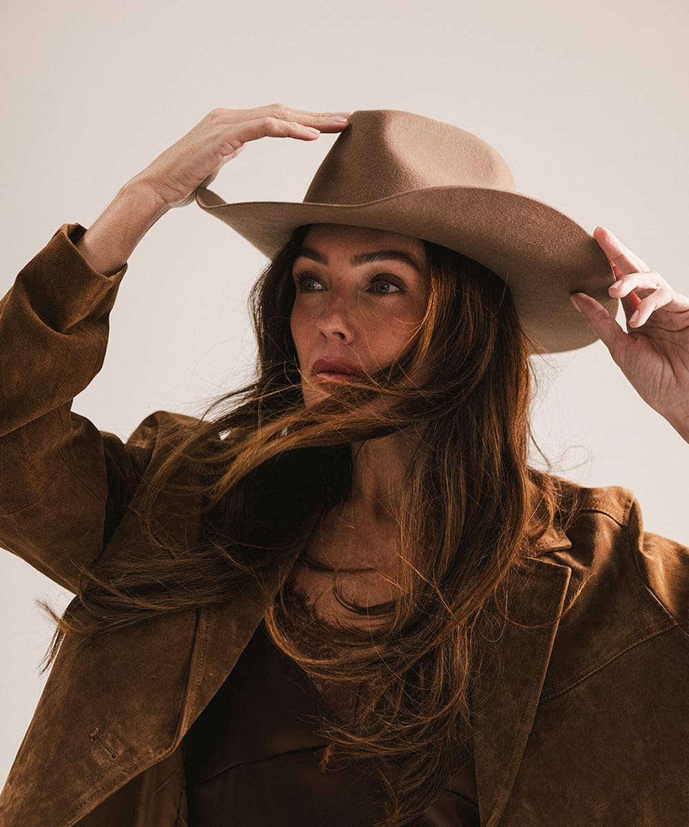 Woman wearing a brown hat and coat against a neutral background