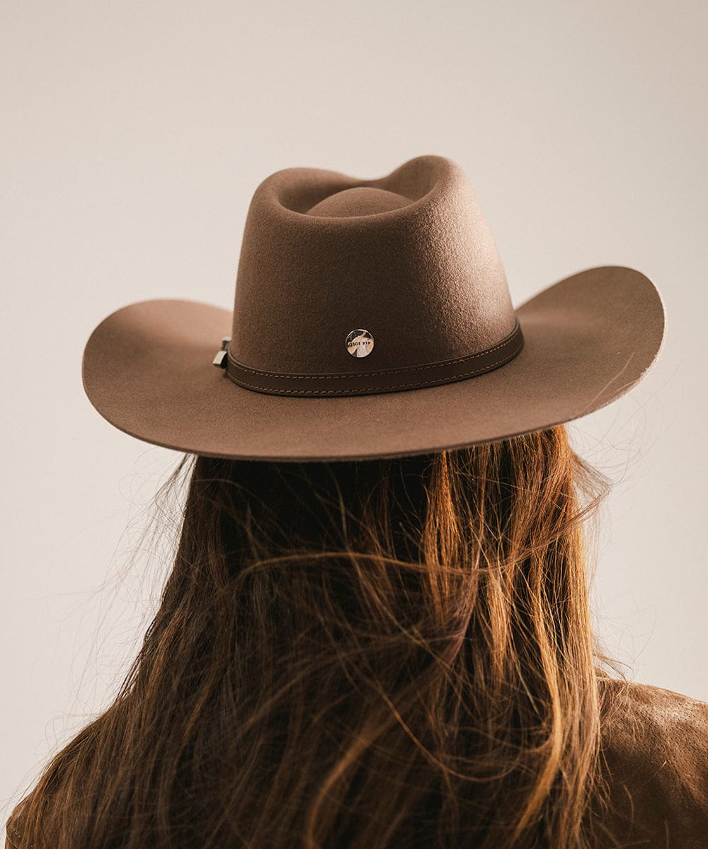 Brown cowboy hat worn by a person with long hair on a plain background