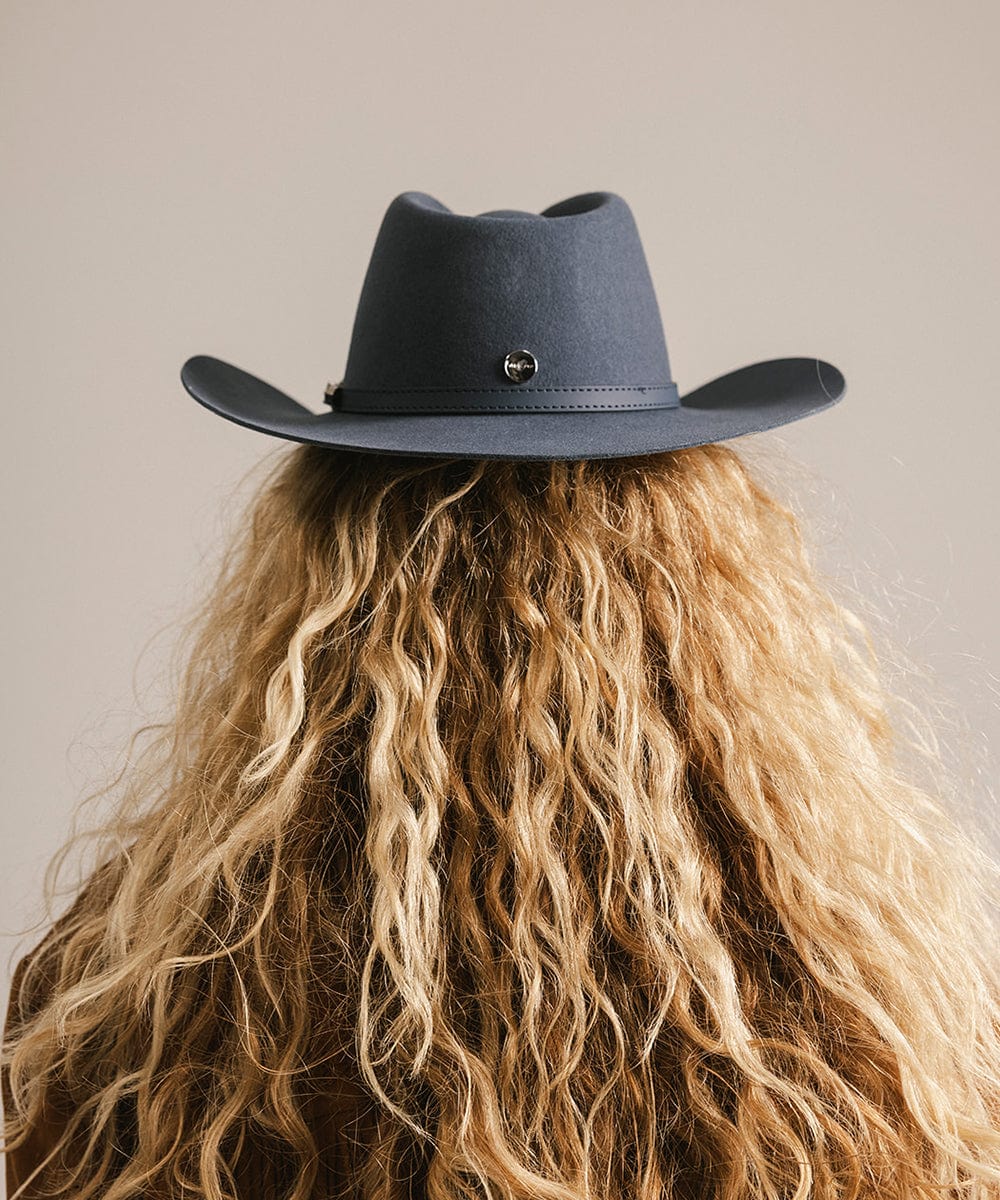 Person wearing a dark blue cowboy hat with a neutral background