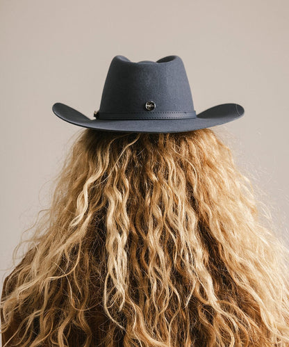 Person wearing a dark blue cowboy hat with a neutral background
