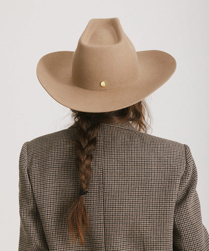 Person wearing a brown cowboy hat and checkered blazer with braided hair on a white background