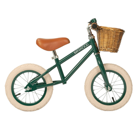 Green balance bike with a wicker basket and brown seat on a white background