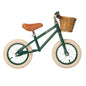 Green balance bike with a wicker basket and brown seat on a white background