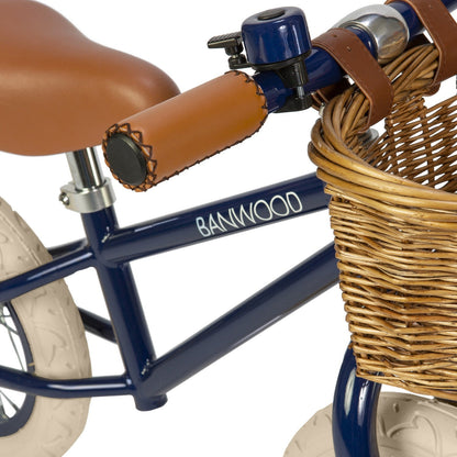 Navy balance bike with brown basket and seat on a white background
