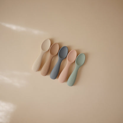 Five colorful spoons on a beige surface