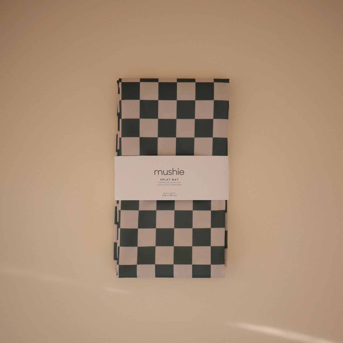 Checkered blanket with 'mushie' branding on a beige background