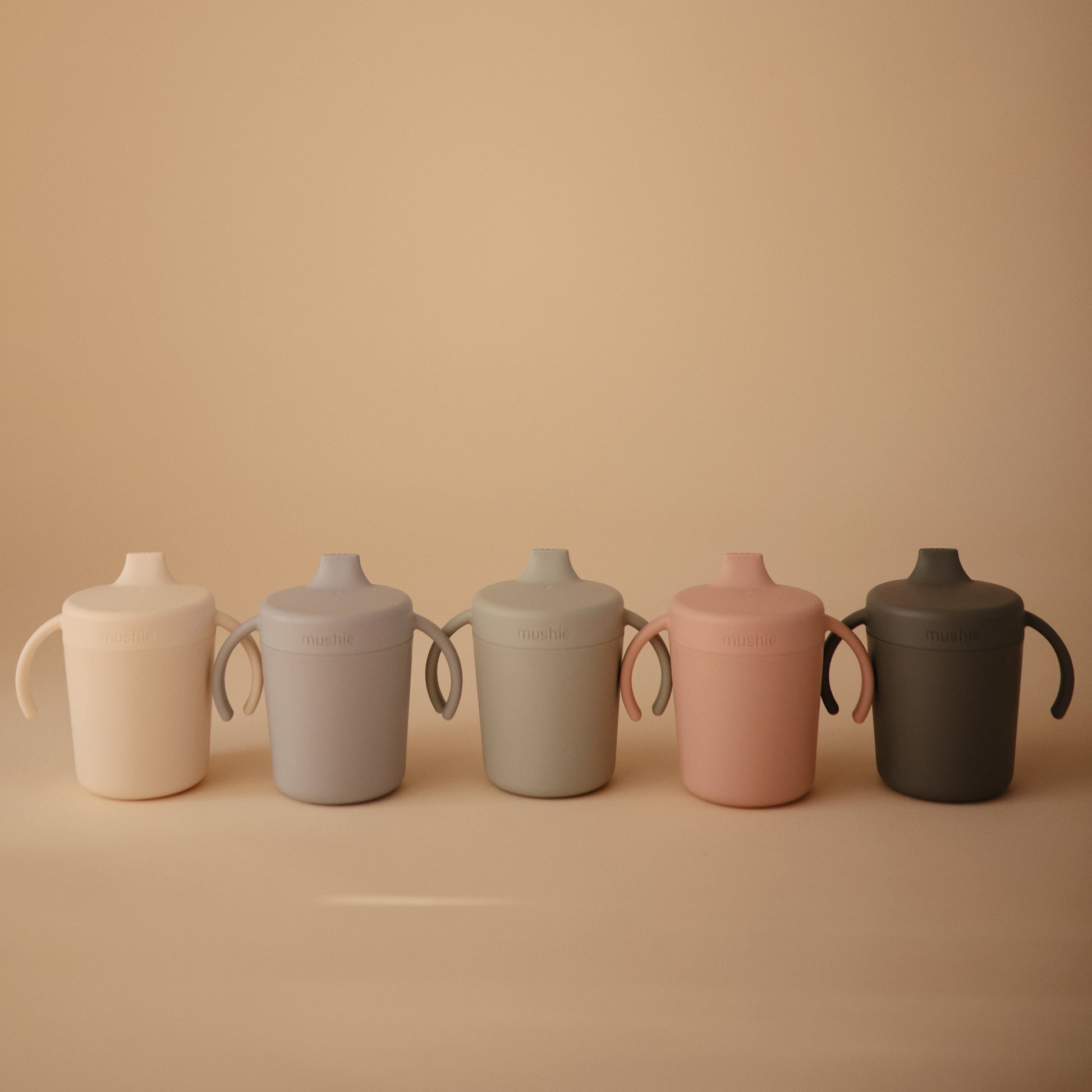 Five ceramic cups in different colors arranged on a beige background