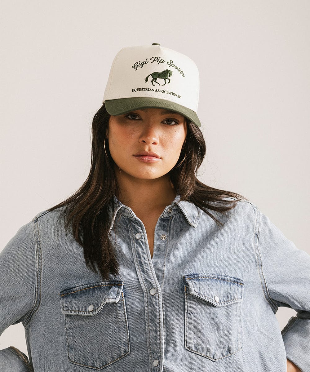 Person wearing a cap with a logo and text, standing against a plain background