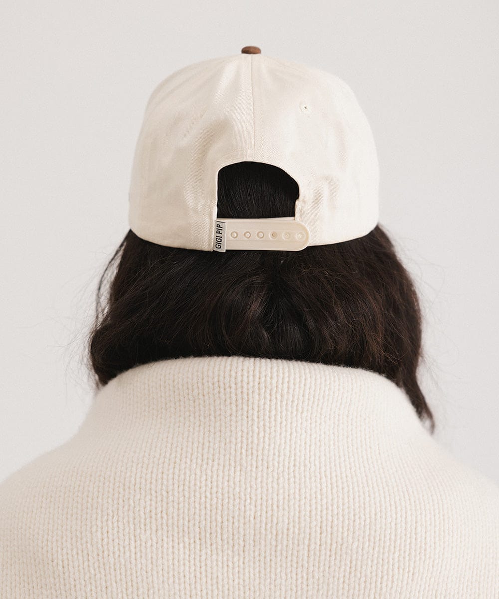 Person wearing a beige cap with a white strap on a plain background