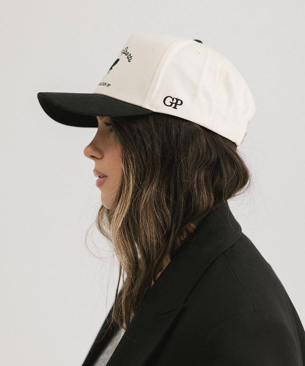 Person wearing a white cap with black brim and logo on a plain background