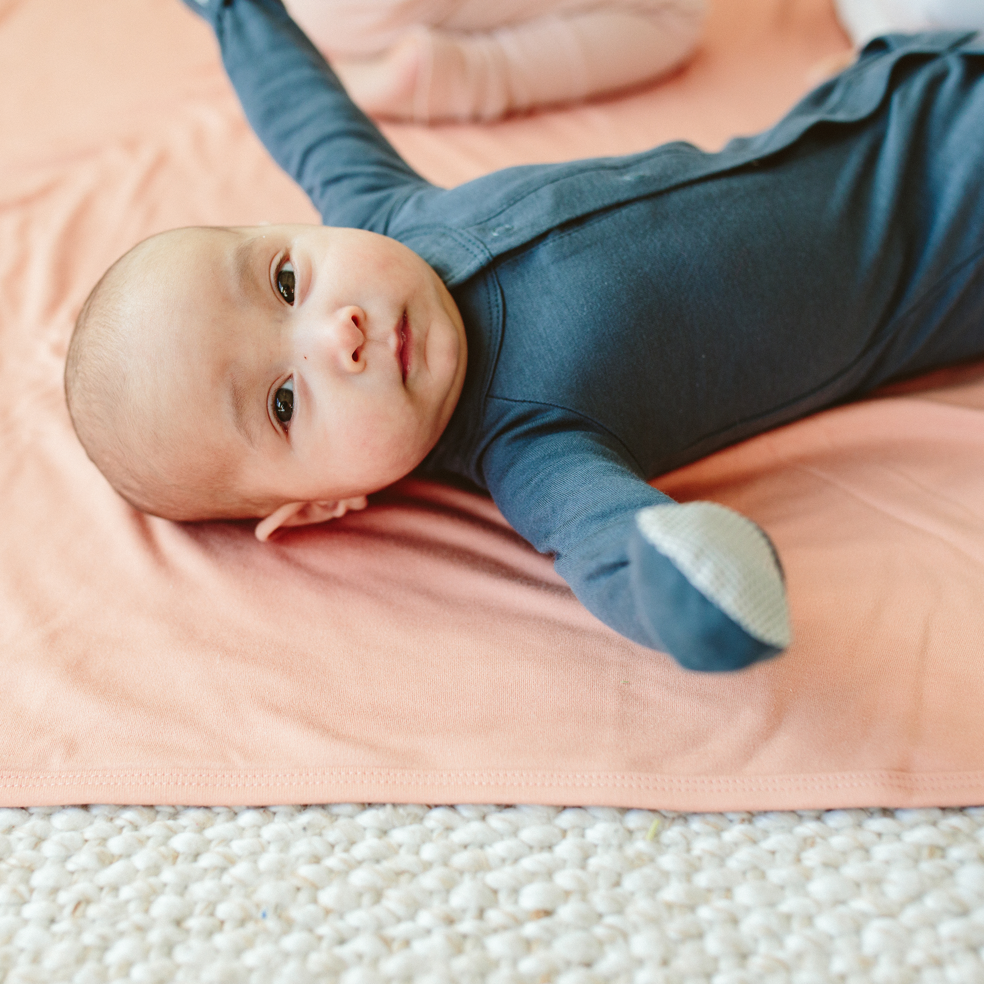 Baby lying on a pink blanket wearing a blue onesie.