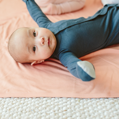 Baby lying on a pink blanket wearing a blue onesie.