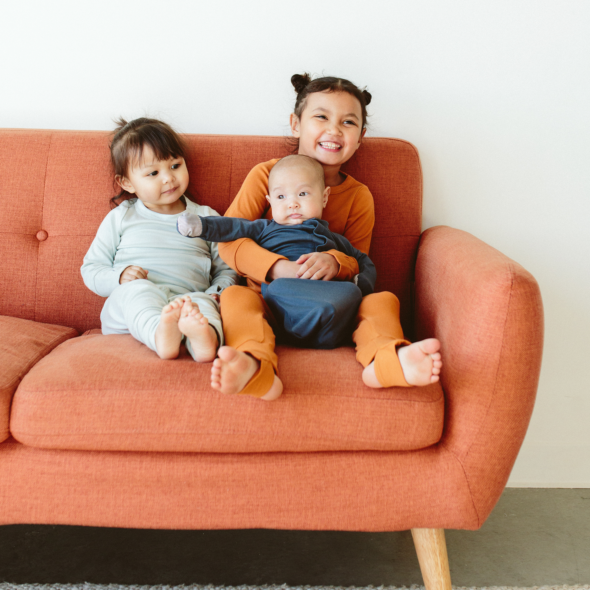 Three children sitting on a red couch, smiling and looking at the camera.