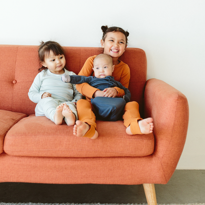 Three children sitting on a red couch, smiling and looking at the camera.