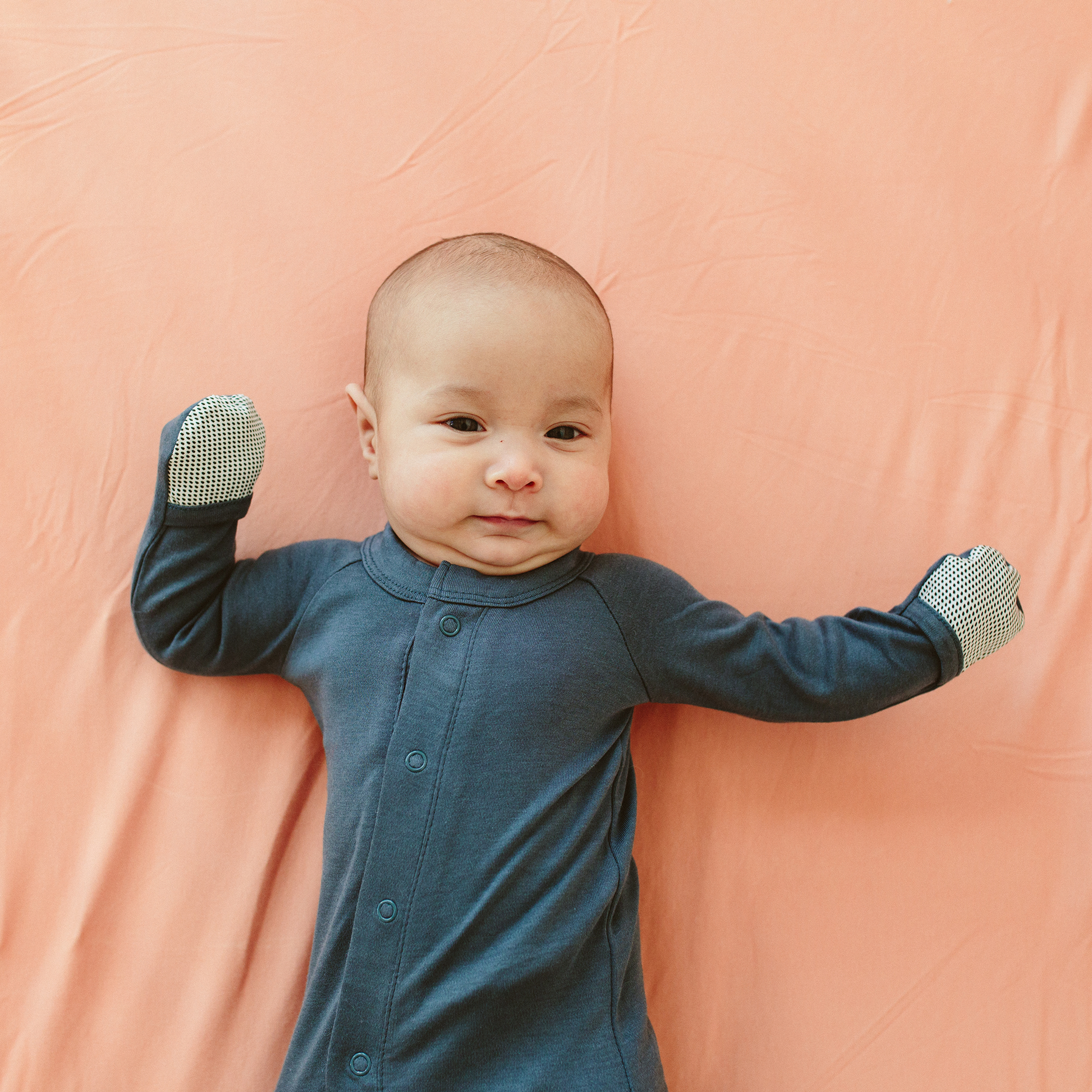 Baby in a blue outfit with polka dot cuffs on a pink background