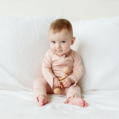Baby in a pink outfit sitting on a white couch holding a wooden toy.