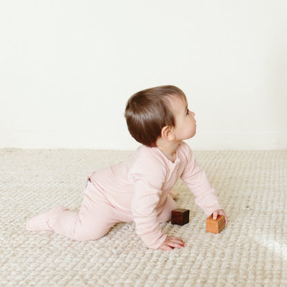 Baby in pink outfit playing with wooden blocks on a light-colored rug.