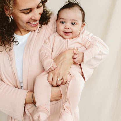 Woman holding a baby in a pink outfit against a neutral background
