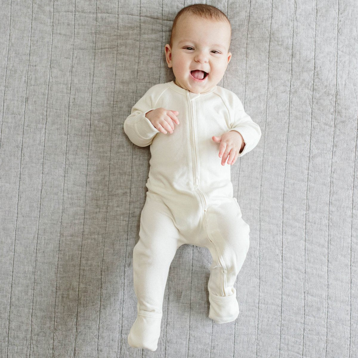 Baby in a white onesie lying on a gray textured surface