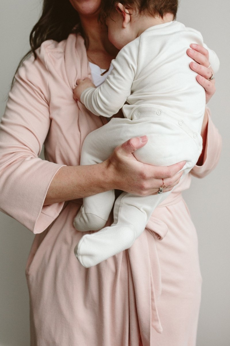 Woman holding a baby wrapped in a white blanket against a neutral background