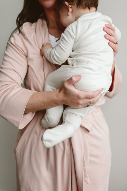 Woman holding a baby wrapped in a white blanket against a neutral background