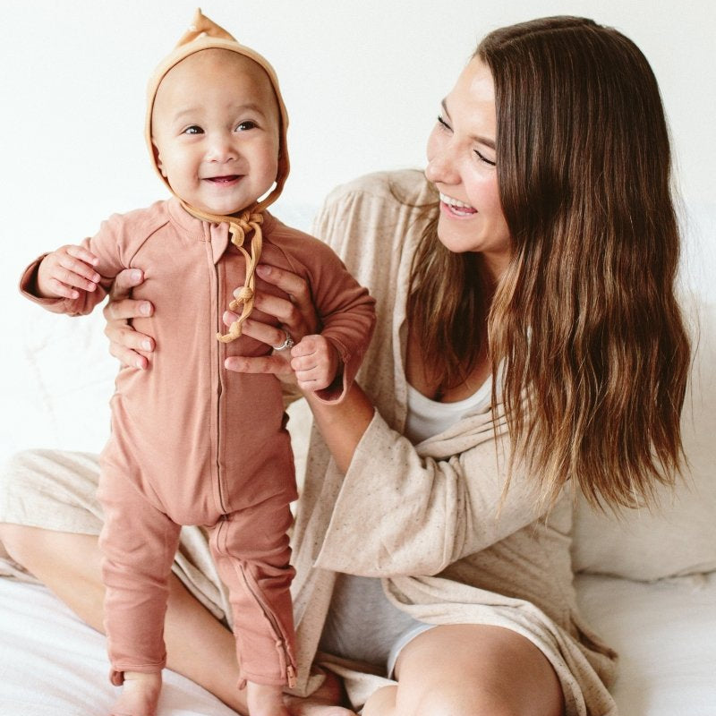 Woman holding a baby in a pink onesie on a white bed