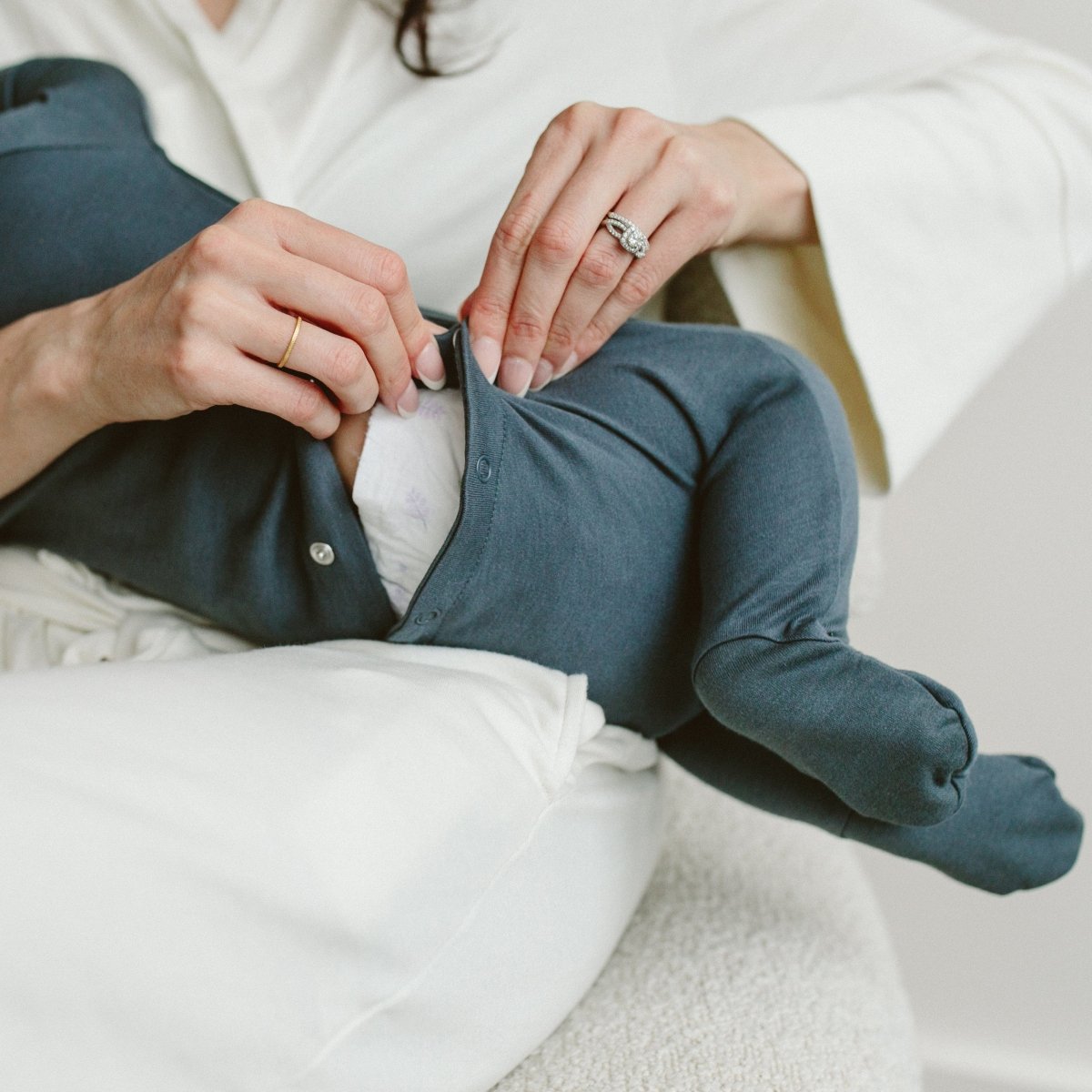 Person holding a baby in blue pants and white shirt on a light background