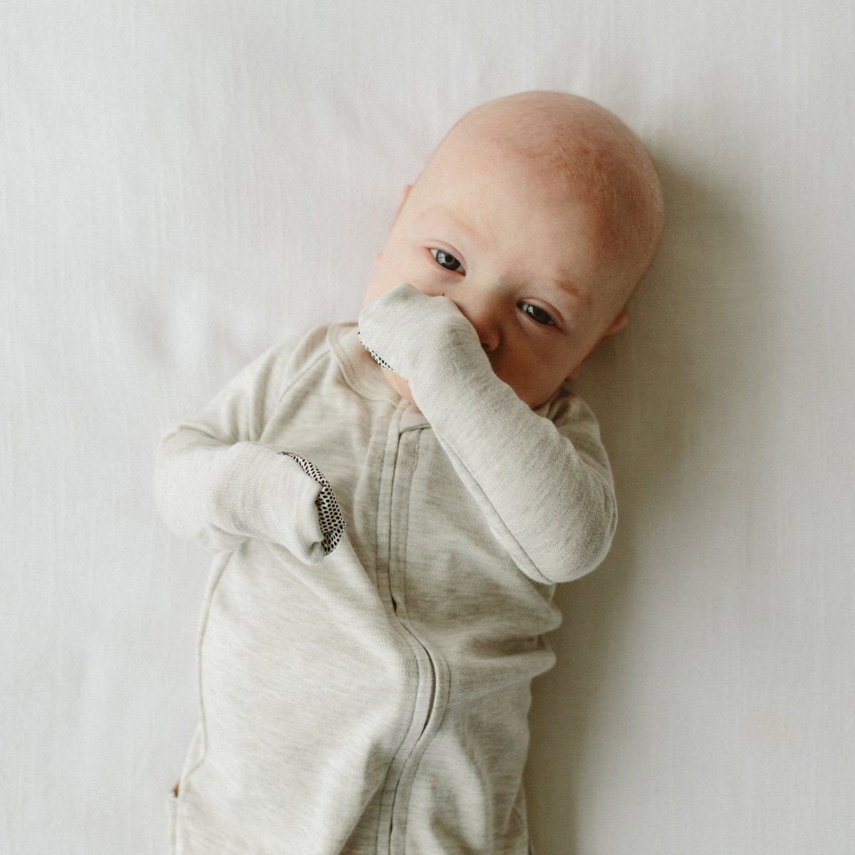 Baby in a light gray onesie lying on a white surface