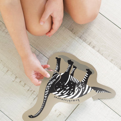 Child's hand holding a zebra-shaped card on a wooden floor