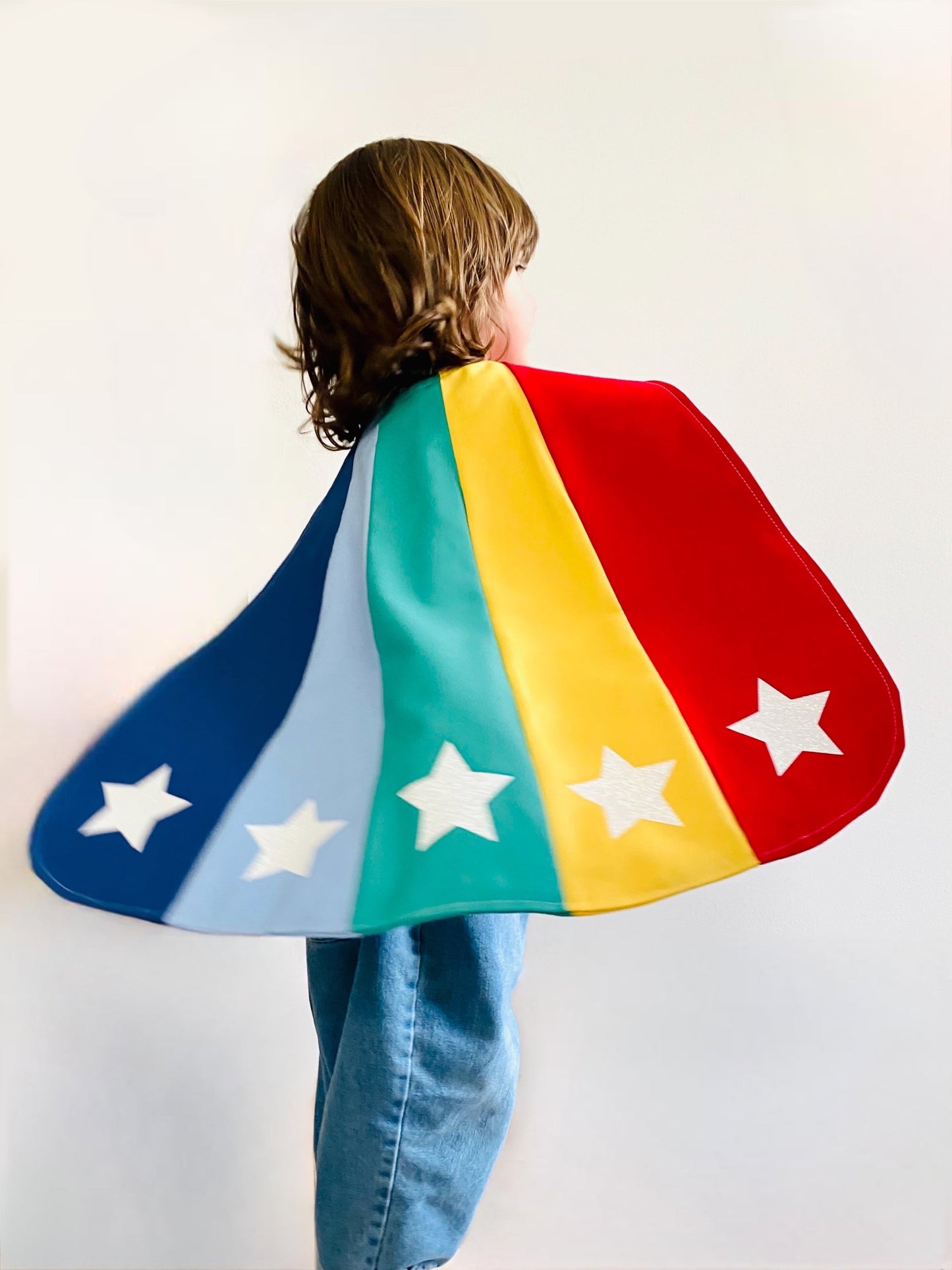 Person wearing a colorful superhero cape with star designs on a plain background