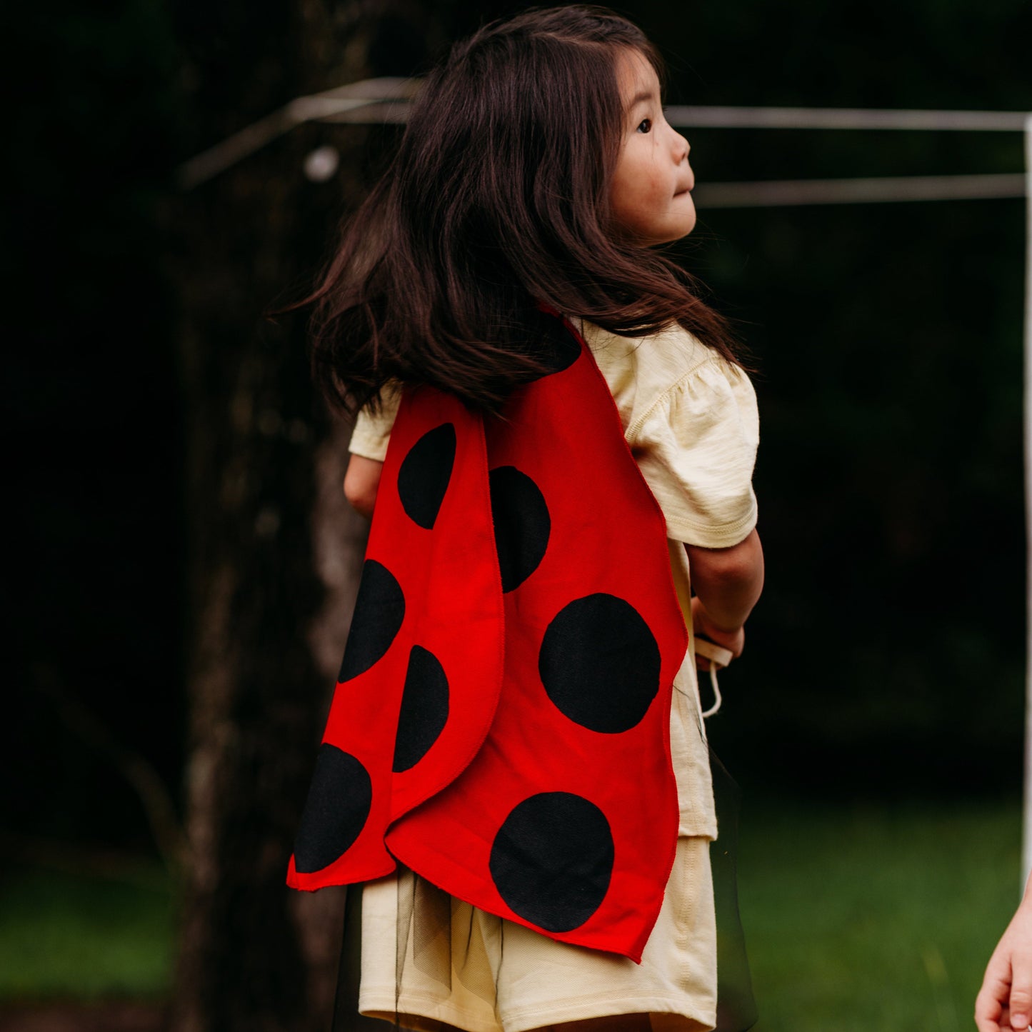 Child wearing a red and black polka dot cape outdoors