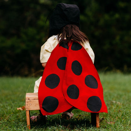 Person wearing a red and black ladybug costume sitting on a wooden stool outdoors.
