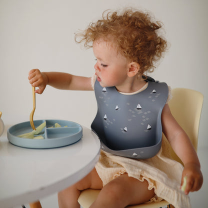 Child eating with a bib and plate on a white table