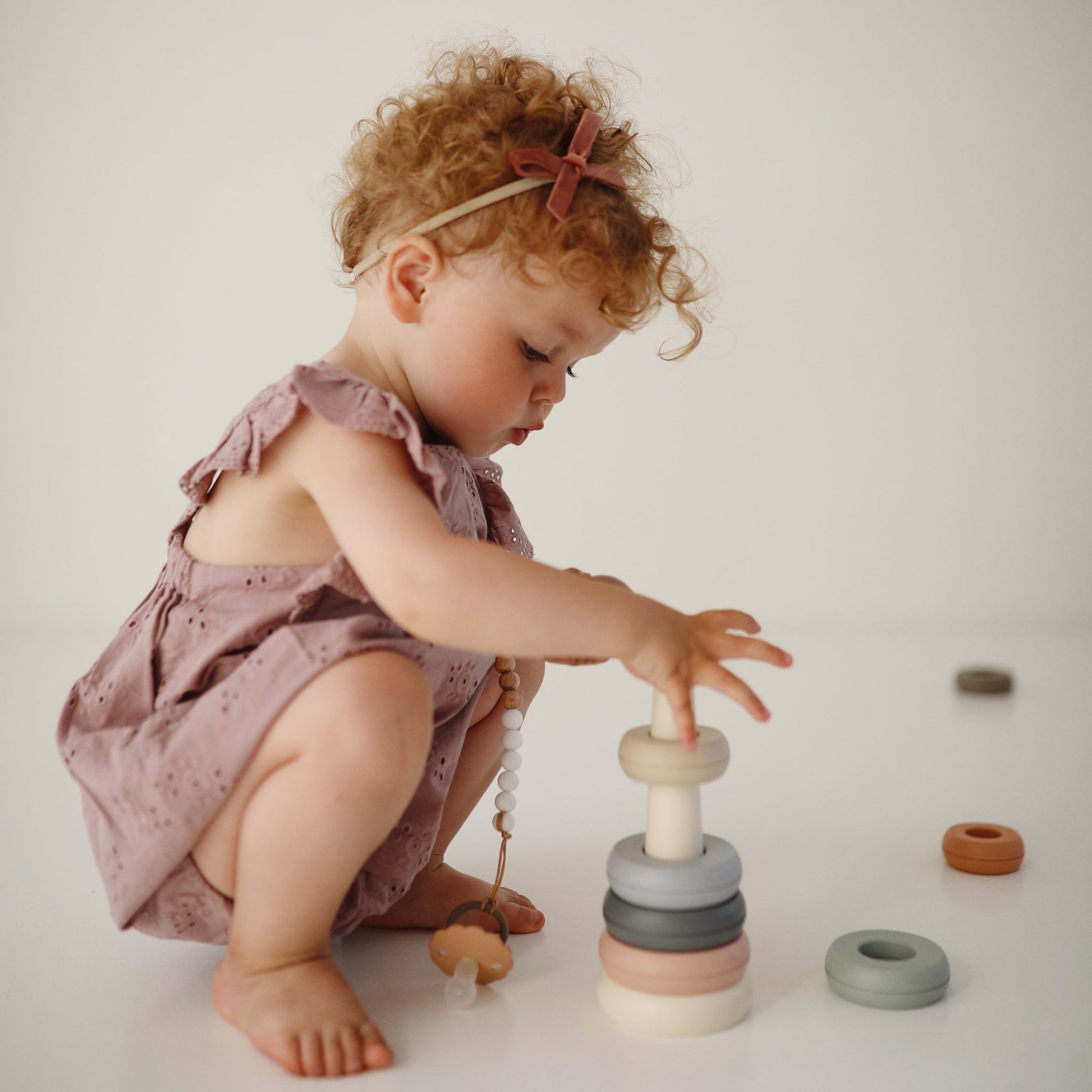 Child playing with a stack of colorful wooden rings on a plain background