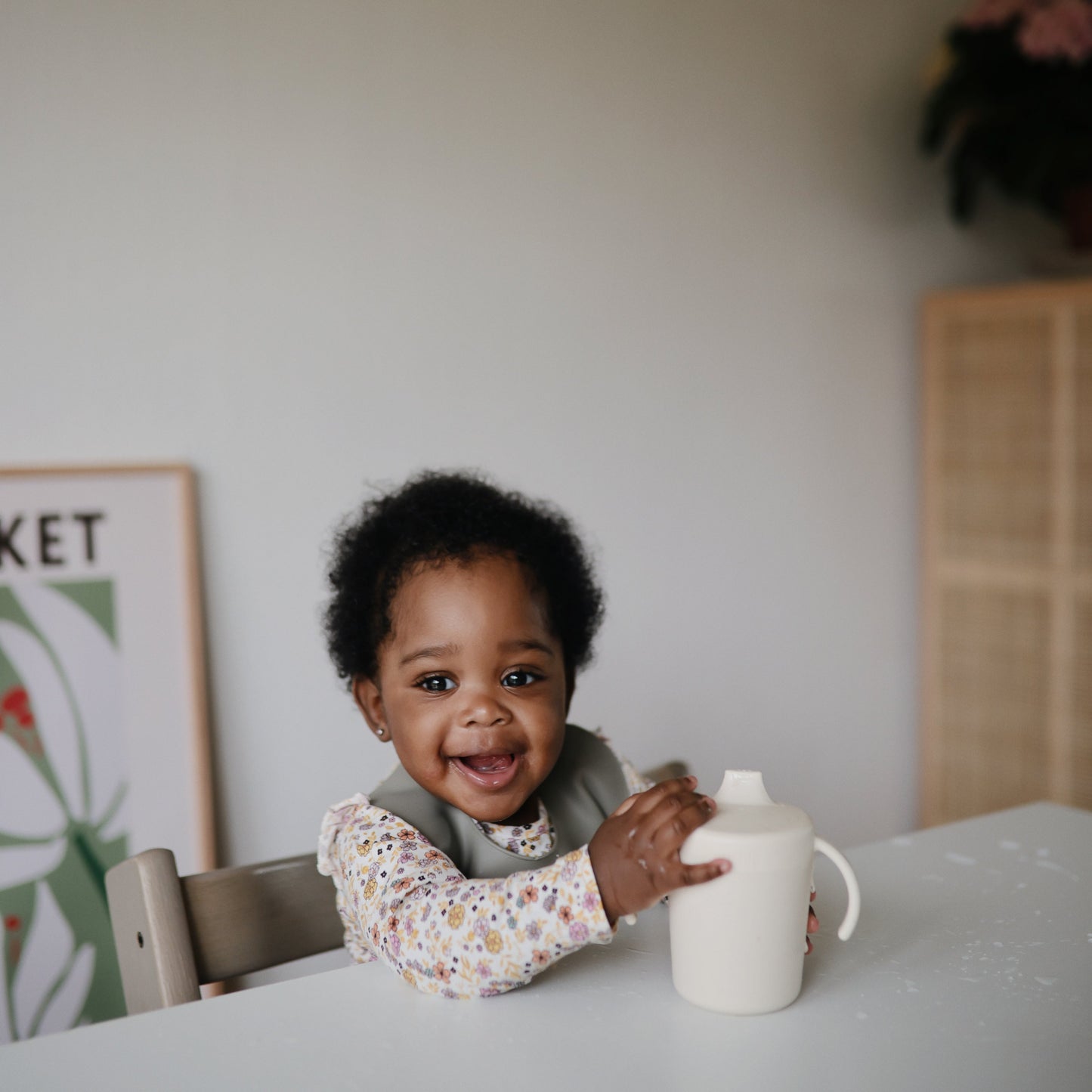 Child holding a white cup in a room with a poster on the wall