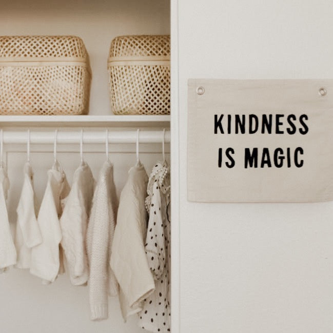 Clothing rack with hanging clothes and a sign that reads 'Kindness is Magic' on a white wall.
