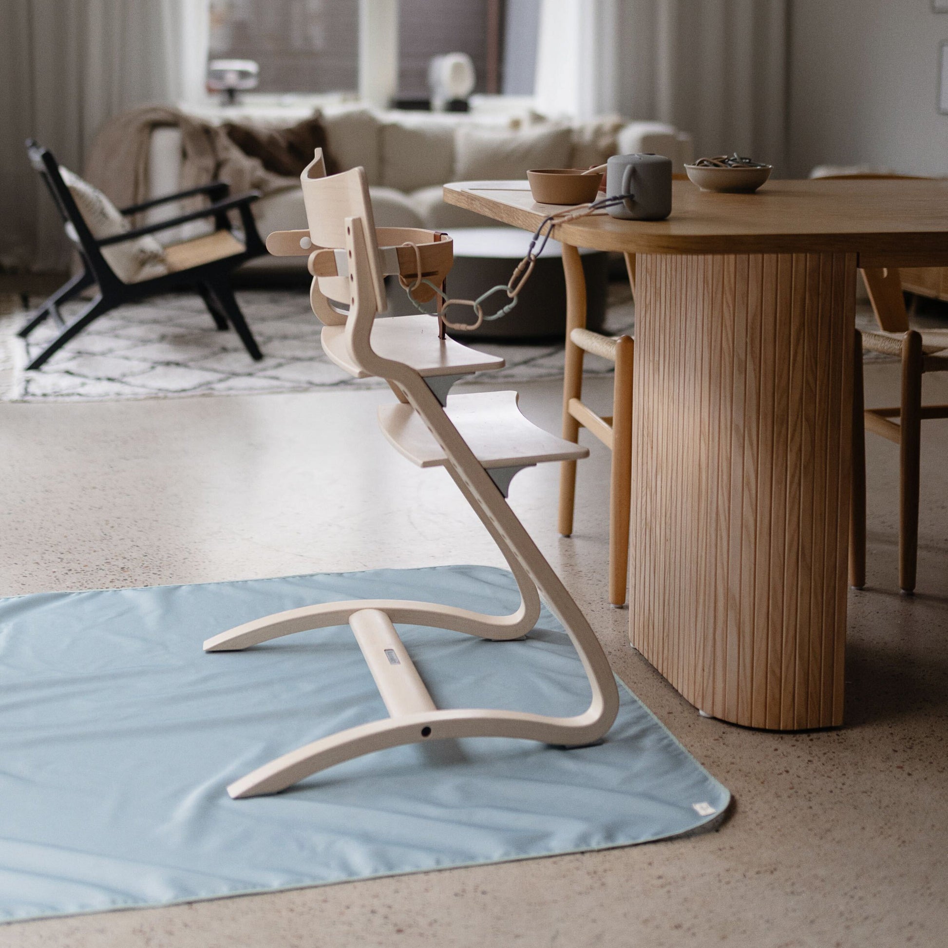 Wooden high chair on a blue mat in a living room with a dining table and chairs.