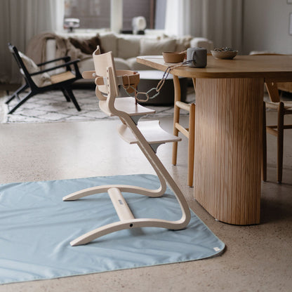 Wooden high chair on a blue mat in a living room with a dining table and chairs.