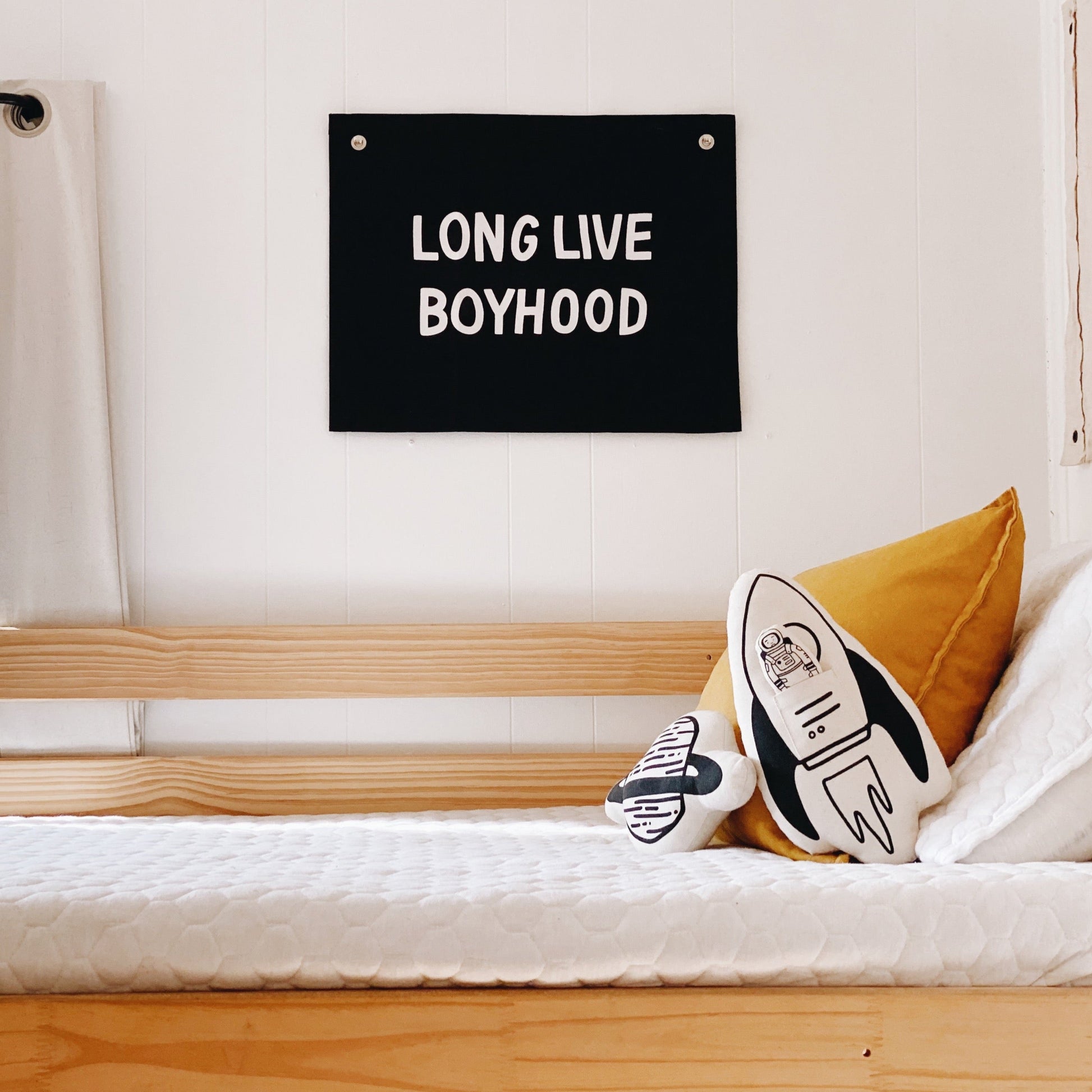 Bedroom with 'LONG LIVE BOYHOOD' sign above a bed with a pillow and plush toy.