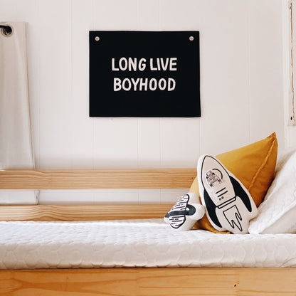 Bedroom with 'LONG LIVE BOYHOOD' sign above a bed with a pillow and plush toy.