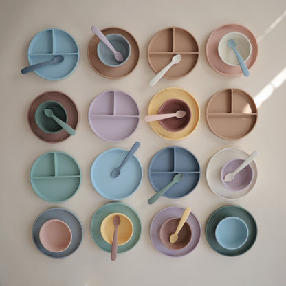 Colorful set of children's plates and spoons arranged in a grid on a light background