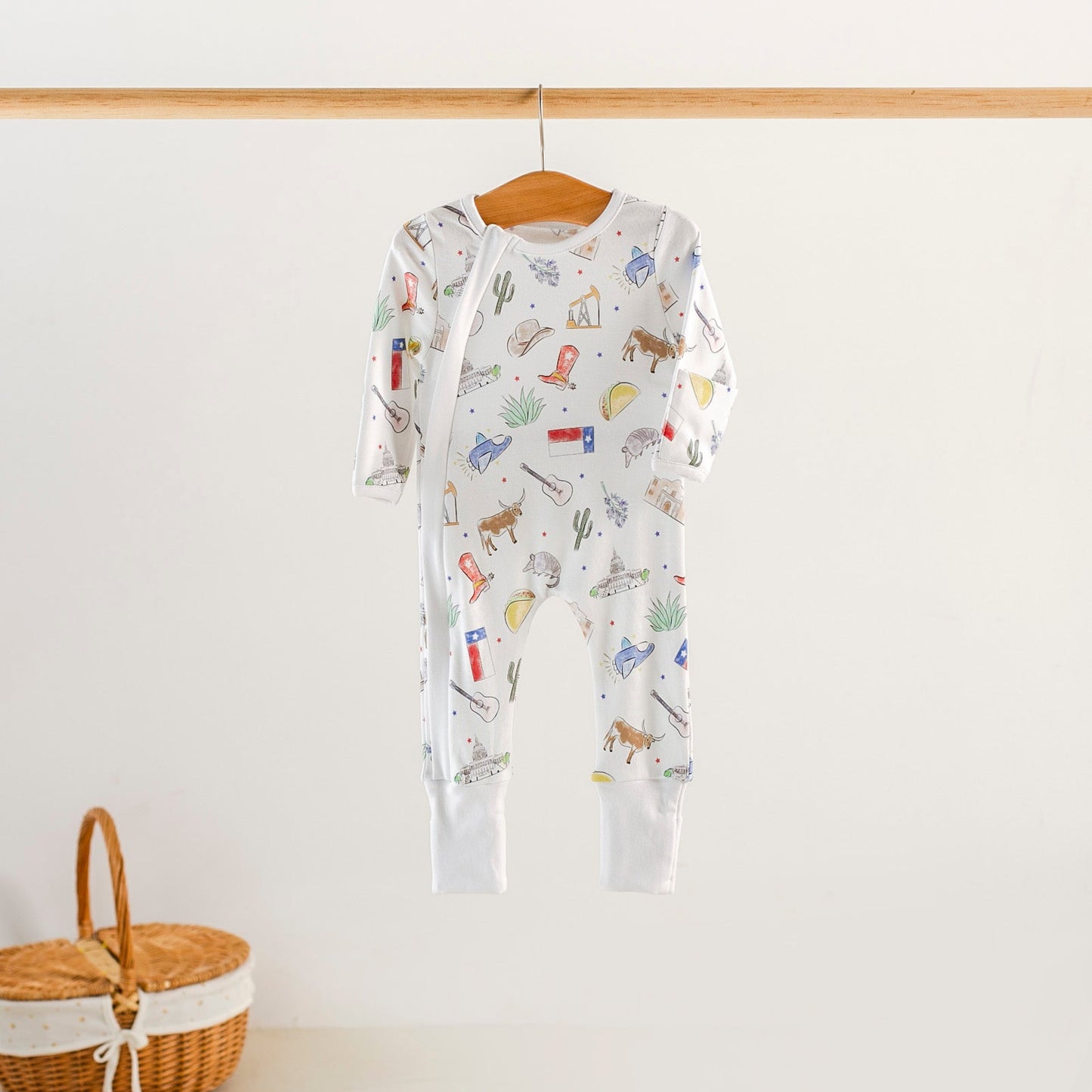 Baby onesie with animal pattern hanging on a wooden hanger against a white wall.