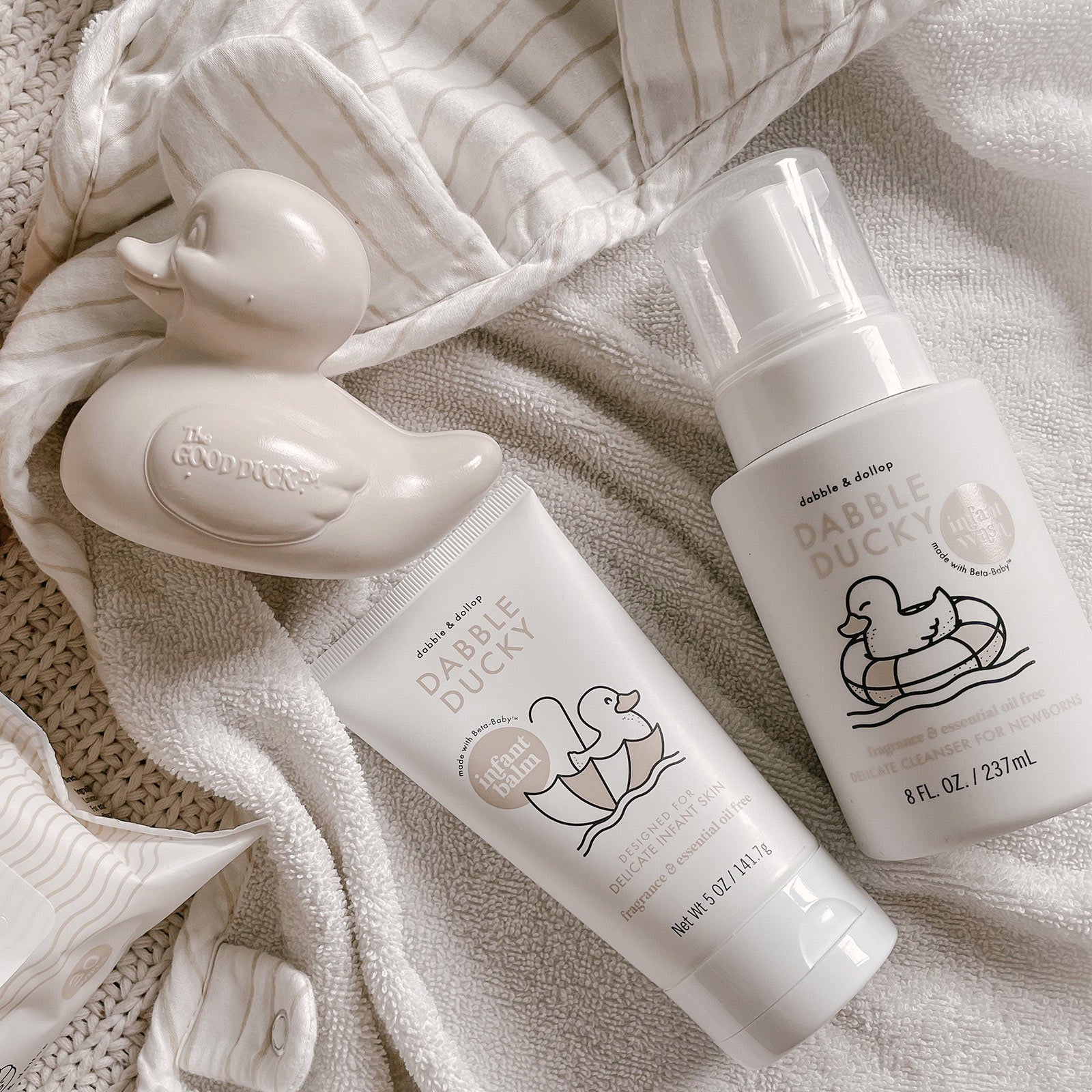 Two bottles of 'Dabble Ducky' baby wash and a rubber duck toy on a textured fabric background.