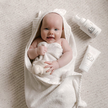 Baby wrapped in a white towel with baby care products on a neutral background