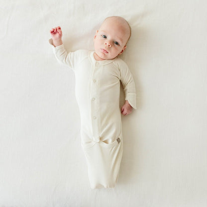 Baby wearing a cream-colored onesie lying on a white surface