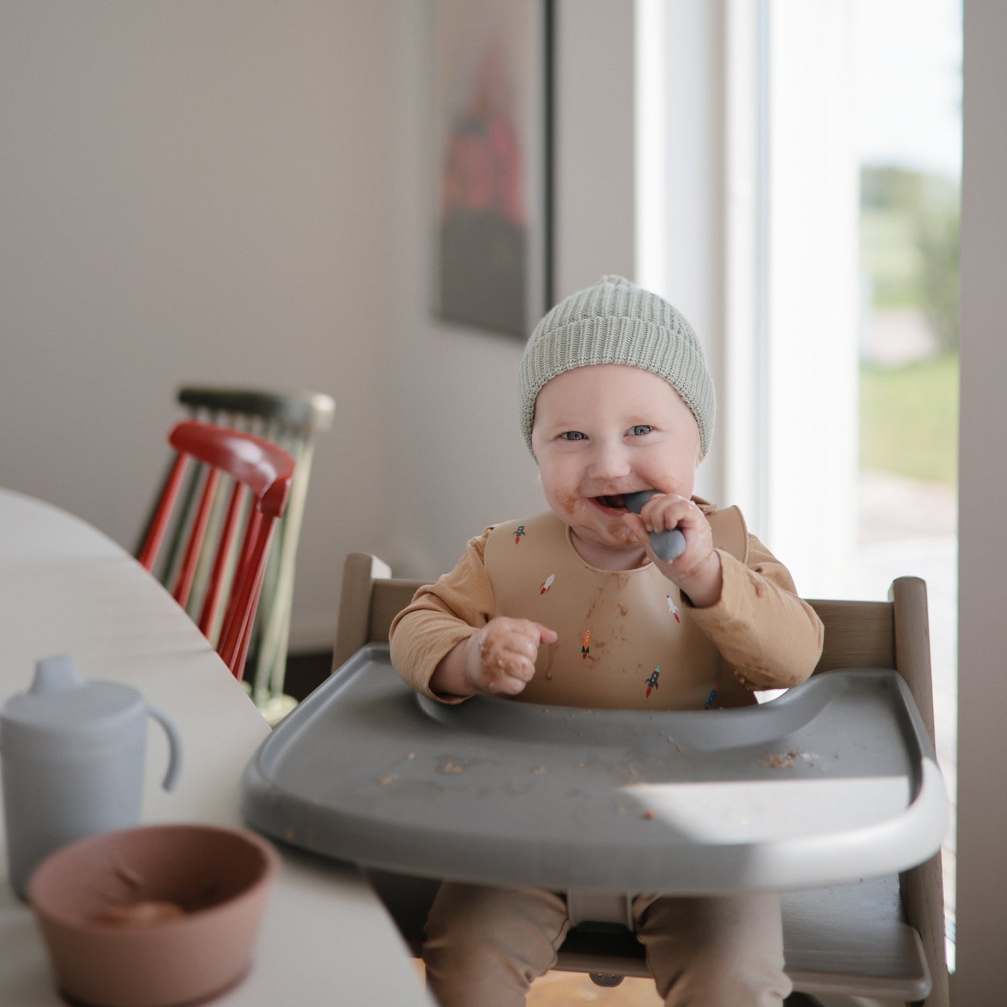 Child in a high chair eating with a spoon in a home setting