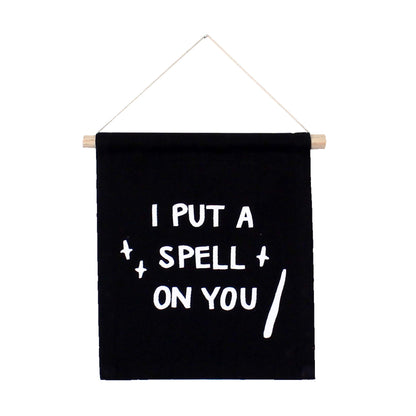 Black banner with white text 'I PUT A SPELL ON YOU' hanging on a white background