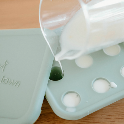 Pouring white liquid into a silicone mold with 'fawn' branding on a wooden surface.